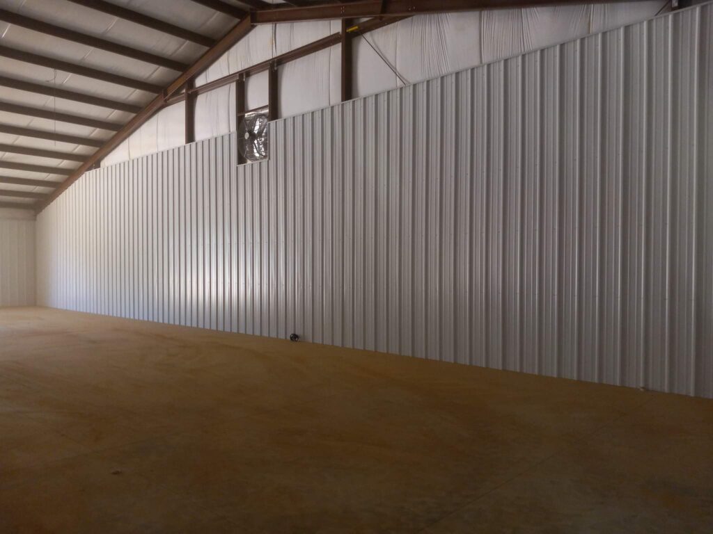 An empty metal building interior features corrugated steel walls, exposed beams, and a polished concrete floor.
