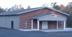 The exterior of a church building and an empty parking lot. There are small crosses on the windows of the church.