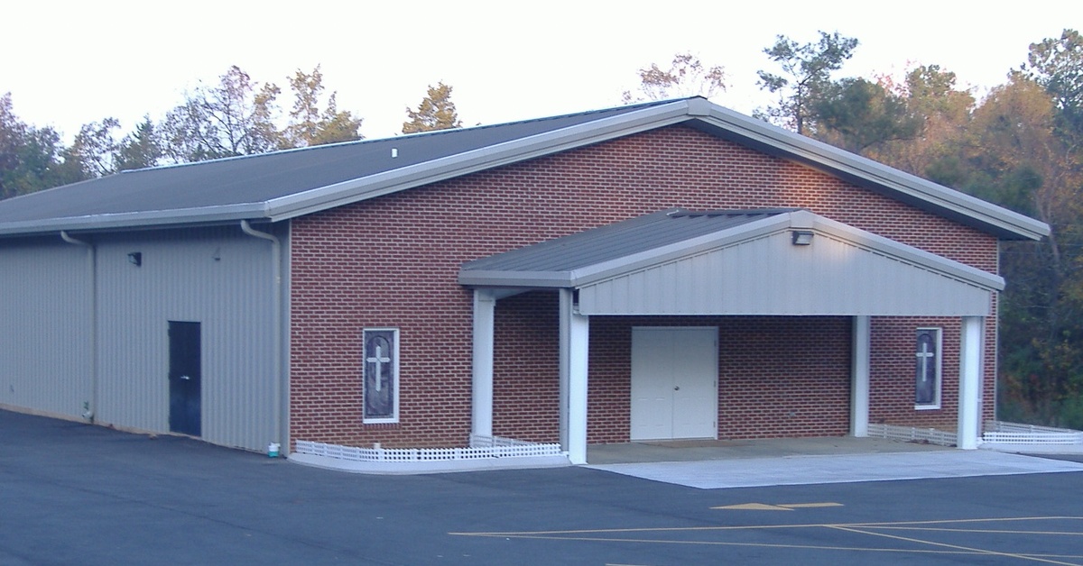 The exterior of a church building and an empty parking lot. There are small crosses on the windows of the church.