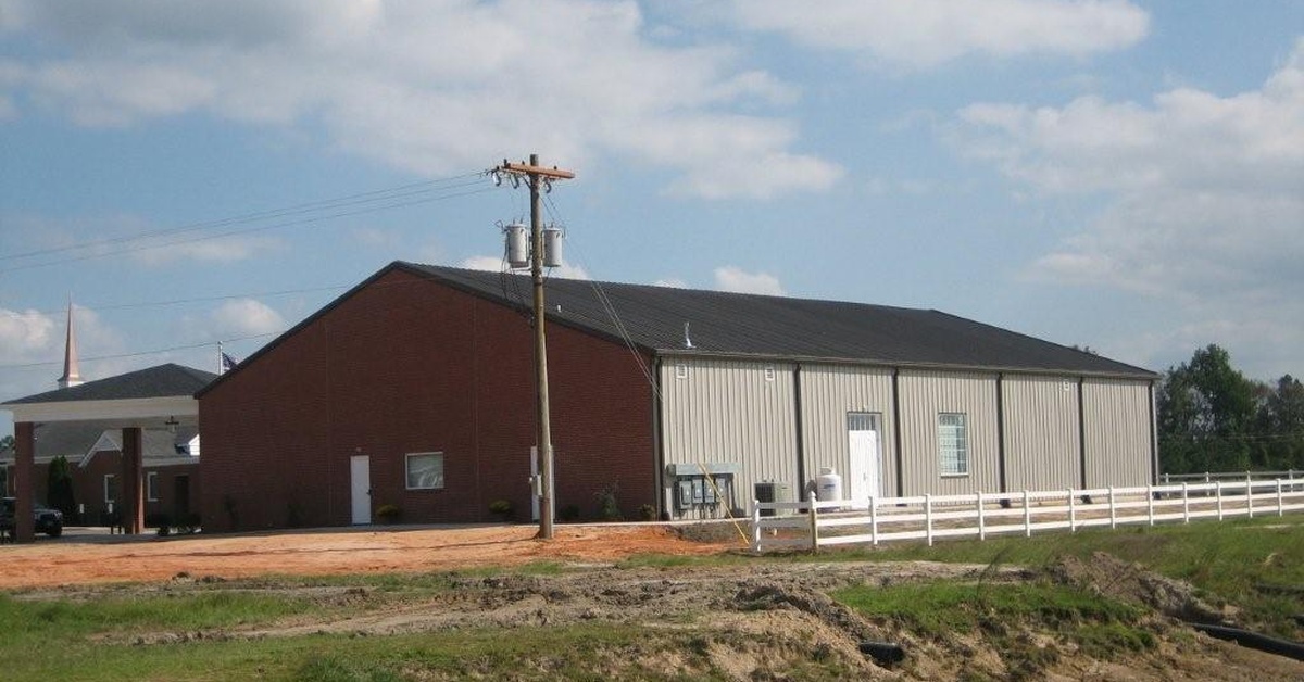 A metal church building seen from a distance. A small white picket fence surrounds the church building.