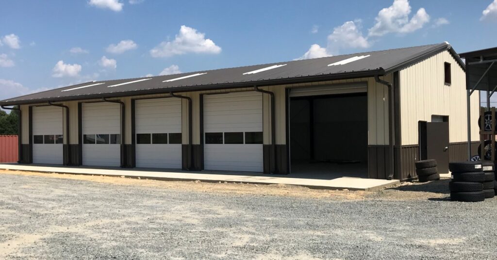 The exterior of a metal building set up as a workshop. There are multiple signs adorning the exterior side walls.