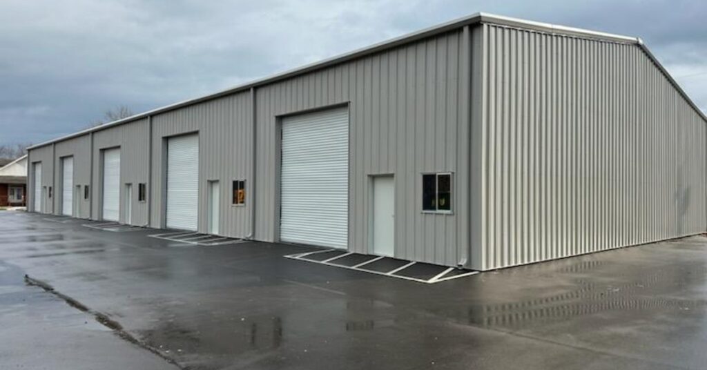 The exterior of a large metal building with multiple garage doors situated in a mostly empty parking lot.