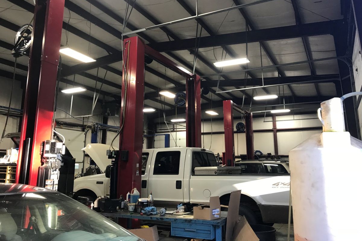 The inside of a garage used for working on vehicles. There are two cars and a pickup truck being worked on.