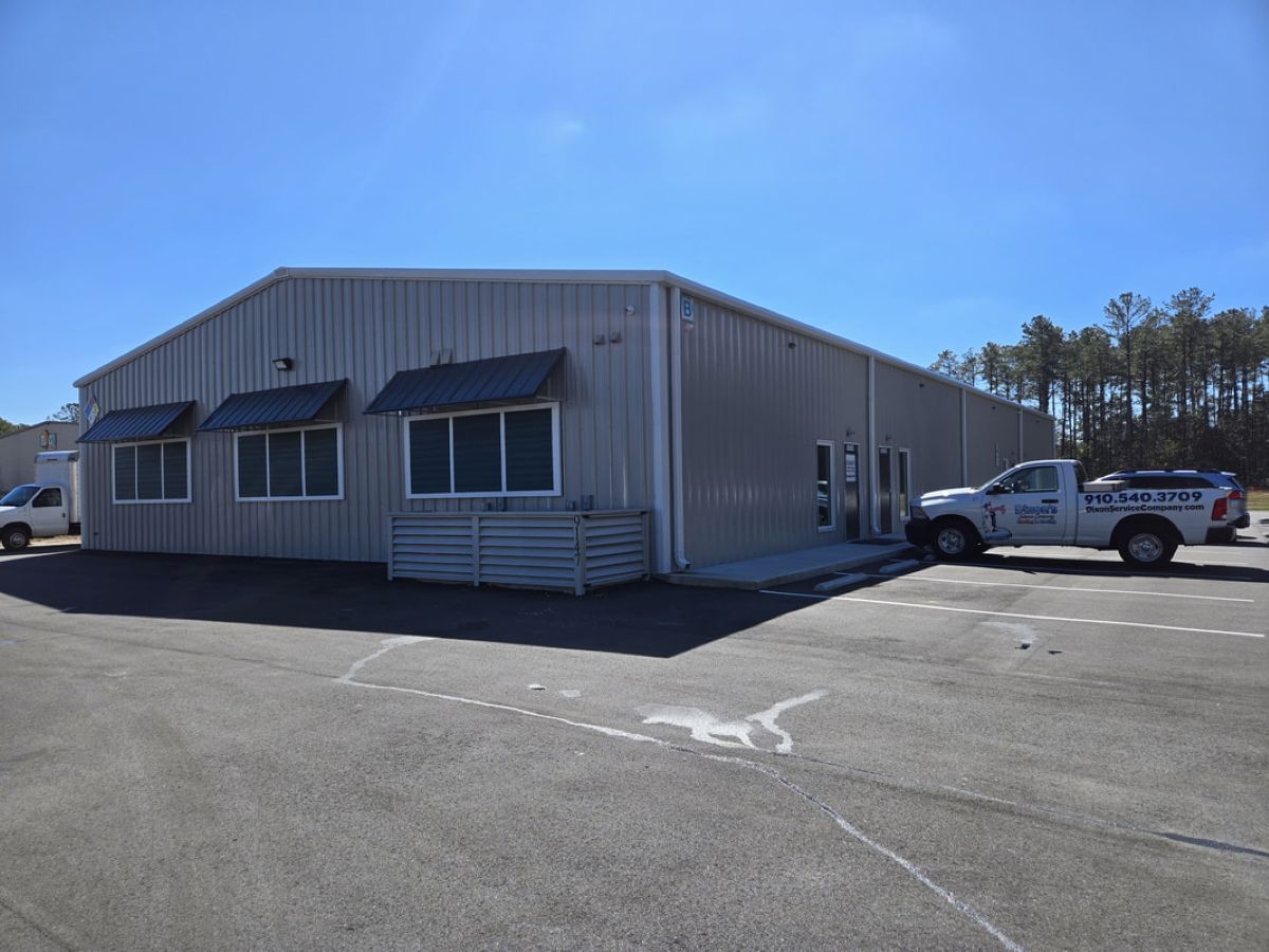 A large metal warehouse in the middle of a parking lot. There are several pickup trucks parked around the entrance.
