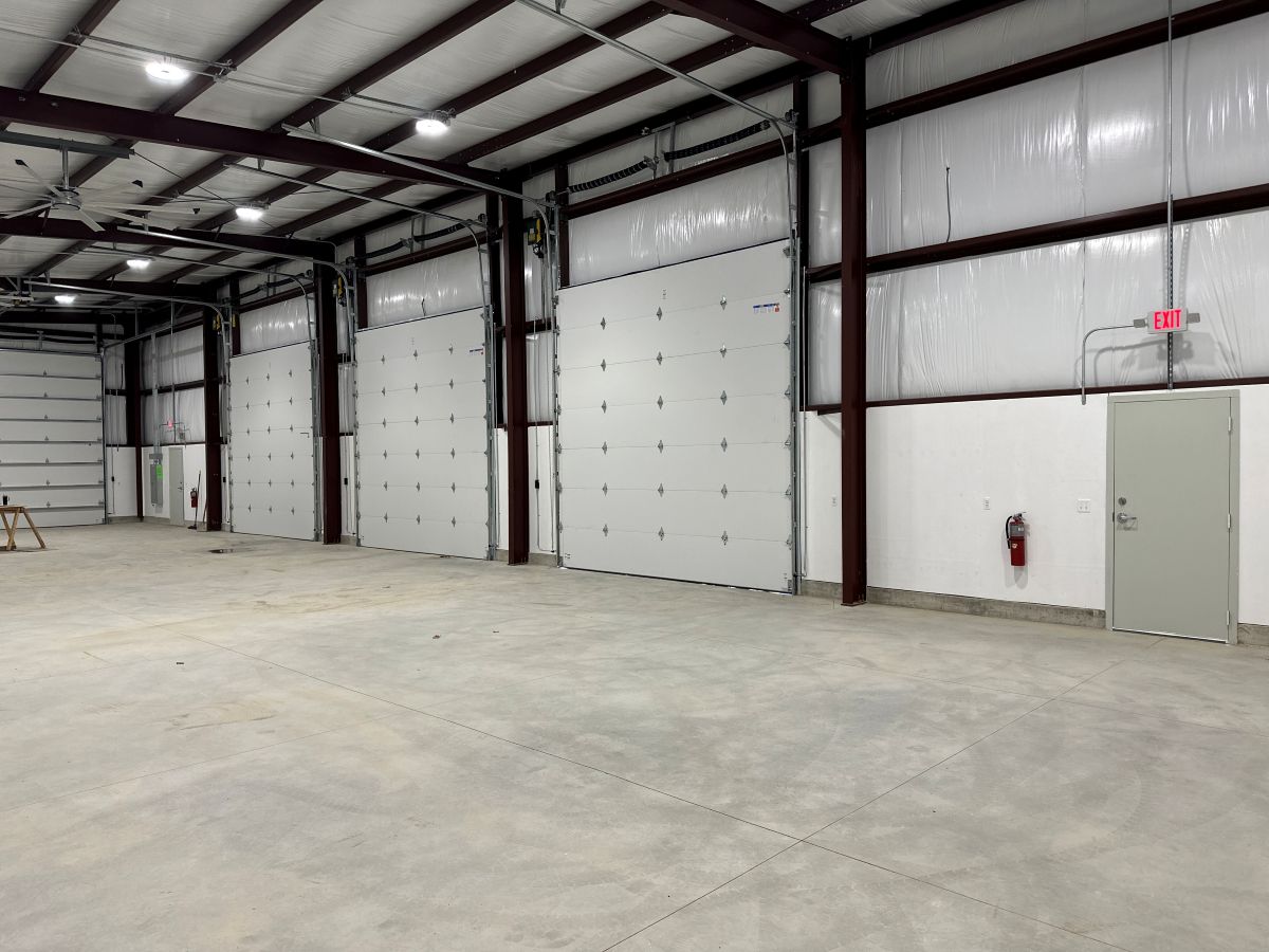 The interior of a large metal warehouse. There are multiple roll-up doors that can allow for vehicles to come in.