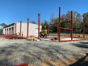 A large metal building under construction. The framework is partially constructed already with other supplies nearby.