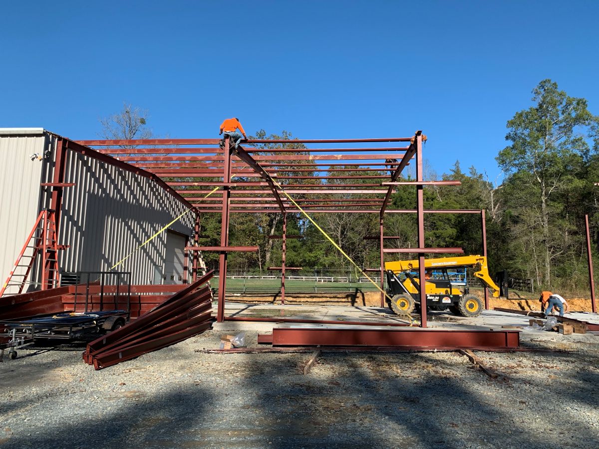 A large metal building under construction. The framework of the building is mostly done, with workers standing on top.