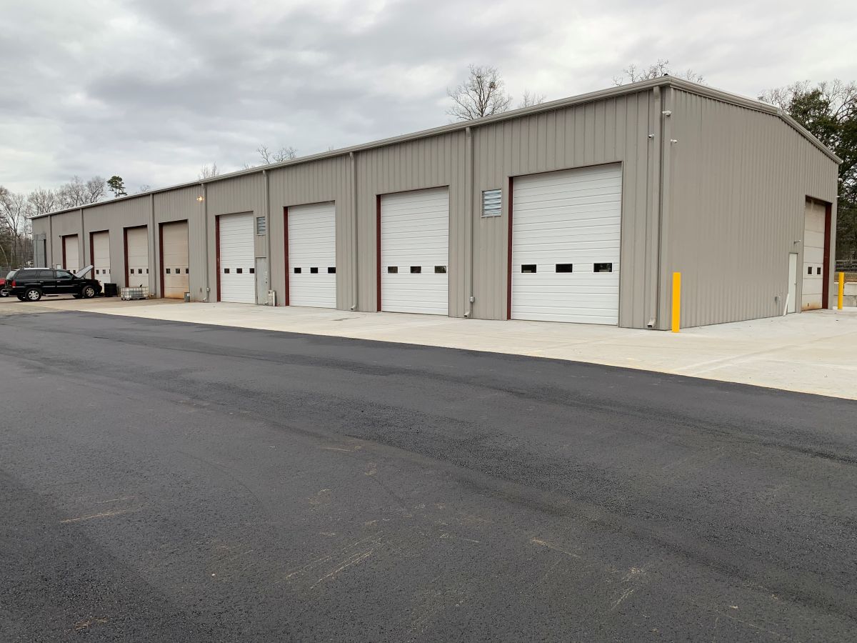 A lineup of several garages made for storage. They each have white roll-up doors and there is a car parked outside one.