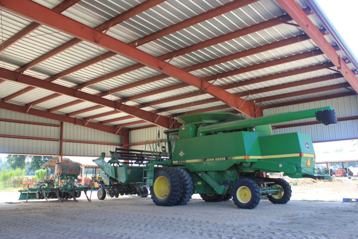The interior of a covered barn for farm vehicles. There is a large, green John Deere crop harvester machine.